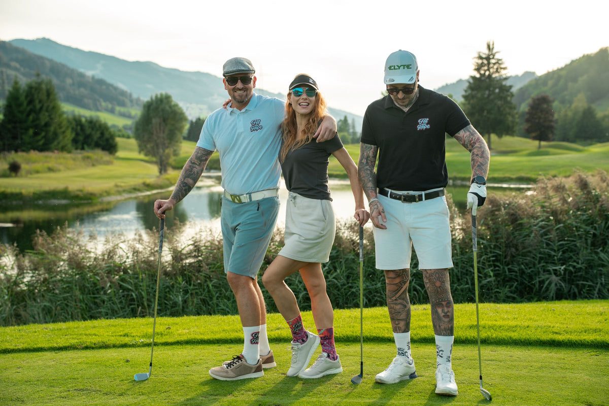 Golfer mitten im Schwung über der Küste, der petrolfarbene Hit and Hope Golfsocken trägt